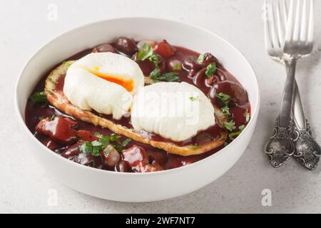 Oeufs en meurette Burgunderpochierte Eier mit Toast in Rotweinsauce mit Pilzen, Zwiebeln und Speck in Nahaufnahme auf einem Teller auf dem Tisch. Horizontal Stockfoto