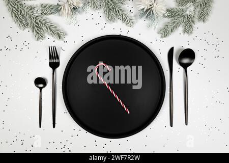 Weihnachtskomposition, schwarzer Teller und Besteck, Tannenzweig, Zuckerrohr, Konfetti mit silbernen Sternen auf weißem Hintergrund. Stockfoto