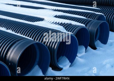 Im Winter sind Abflussrohre aus schwarzem Kunststoff ordentlich auf der verschneiten Oberfläche angeordnet. Stockfoto