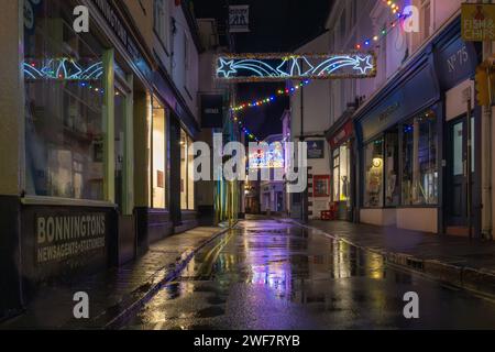 Blick auf die Fore Street auf einem nassen, ruhigen Wintergeschehen mit den Weihnachtslichtern über dem Himmel, die sich in den Pfützen am Boden spiegeln. Stockfoto