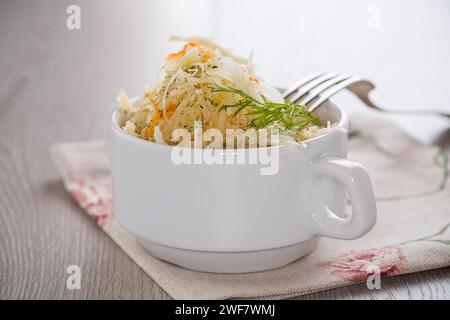 Sauerkraut mit Karotten und Gewürzen in einer weißen Schüssel auf einem hellen Holztisch. Stockfoto