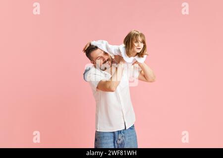 Fröhlicher Vater und Kind, das fantasievolle Spiele spielen, simulieren das Fliegen vor pinkfarbenem Hintergrund. Das Konzept des Internationalen Tages des Glücks Stockfoto