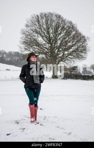 Ein einsames Weibchen wandert leise durch eine verschneite Winterlandschaft, gekleidet mit Stiefeln, Mantel, Hut und Schal. Stockfoto