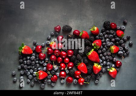 Frische gemischte Beeren und Kirschen von oben auf einer grauen Oberfläche mit Kopierraum Stockfoto