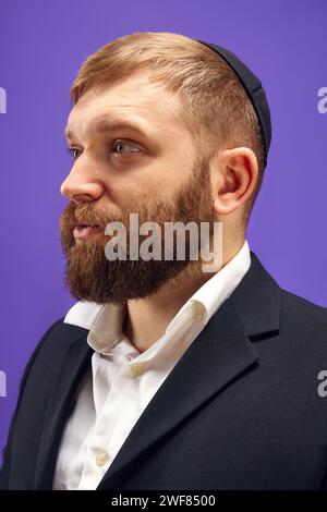 Porträt eines bärtigen jungen jüdischen Mannes in Jarmulke, der vor purpurrotem Atelierhintergrund posiert Stockfoto