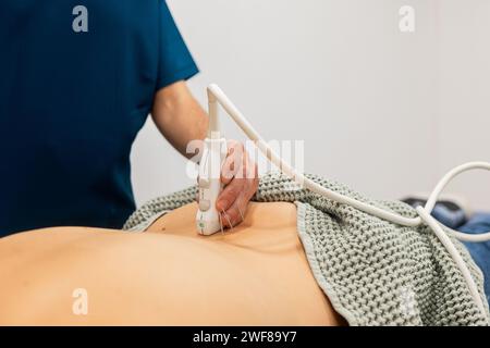 Ein medizinisches Fachpersonal führt einen Ultraschall im Bauchbereich eines Patienten durch, wobei ein Schallkopf verwendet wird, um die Haut zu scannen Stockfoto