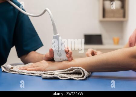 Ein medizinisches Fachpersonal wendet eine Ultraschalltherapie an, indem es ein tragbares Gerät am Arm eines Patienten verwendet, der auf einer mit einem Handtuch bedeckten Oberfläche aufliegt Stockfoto