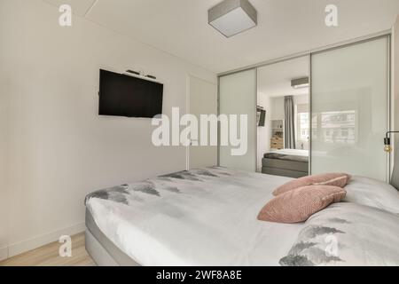 Modernes Schlafzimmer mit großem Bett und Spiegelschrank, minimalistischer Einrichtung und Flachbildfernseher. Stockfoto