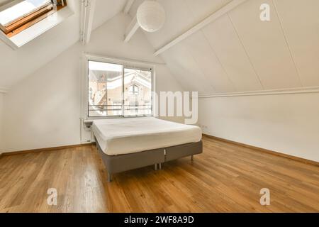 Helles und luftiges Schlafzimmer im Dachgeschoss mit minimalistischem Design, großem Fenster und Holzfußboden. Stockfoto