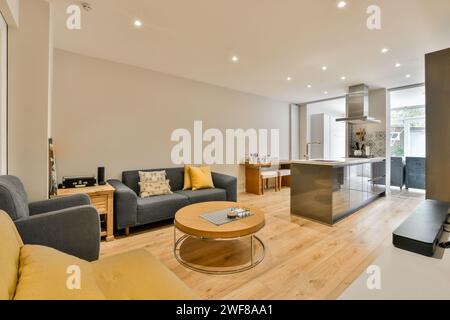 Ein geräumiges und modernes Wohnzimmer, das nahtlos in eine offene Küche übergeht, mit komfortablen Möbeln, Hartholzböden und hellem Licht Stockfoto