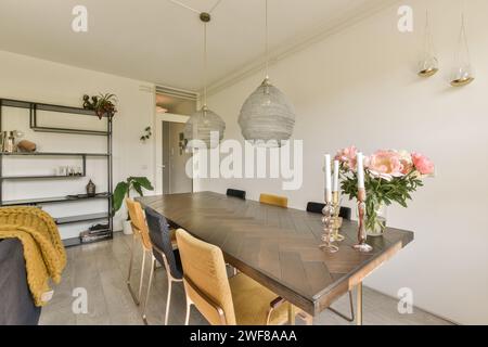 Ein gut beleuchteter, moderner Speisesaal mit dunklem Holztisch, stilvollen Stühlen und eleganten Hängelampen. Stockfoto