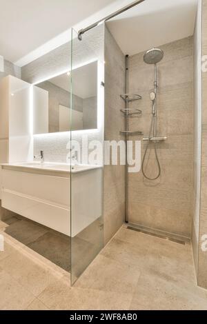 Ein elegantes, modernes Badezimmer mit verglaster Duschecke und weißem Kosmetikbereich mit großem Spiegel und moderner Beleuchtung. Stockfoto