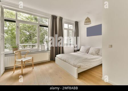 Ein gut beleuchtetes Schlafzimmer mit einem großen Fenster mit Blick auf das Grün, einem komfortablen Doppelbett, Holzfußboden und minimalistischer Einrichtung. Stockfoto