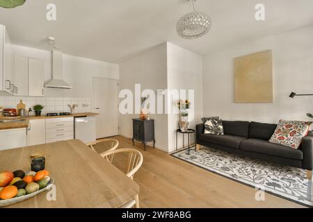 Ein gemütliches und modernes Wohnzimmer fügt sich nahtlos in eine voll ausgestattete Küche mit stilvollem Sofa, gemustertem Teppich und warmen Holztönen ein. Stockfoto