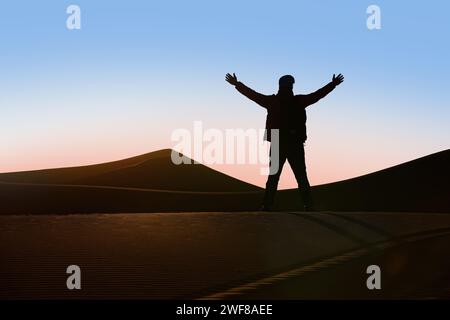 Rückansicht einer nicht erkennbaren Silhouette eines Abenteurers mit triumphalen Armen vor einem Sonnenuntergang in der Merzouga-Wüste, Erg Chebb Stockfoto