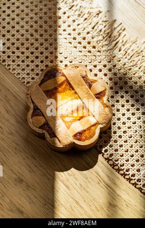 Ein sonnendurchflutetes italienisches Pastiera Napoletana wirft verspielte Schatten auf eine Holzfläche, umgeben von Osterelementen. Stockfoto