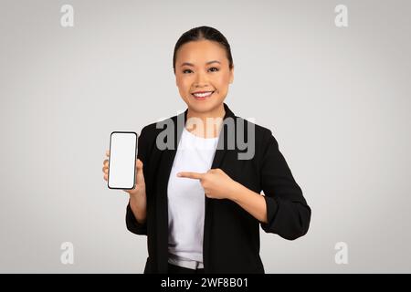 Lächelnde asiatische Geschäftsfrau präsentiert ein Smartphone mit einem leeren Bildschirm Stockfoto
