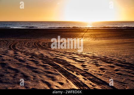 Spuren von Reifenspuren im Sand bei Sonnenaufgang. Konzept von Ziel oder Pfad. Stockfoto