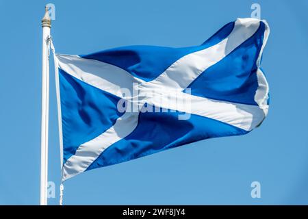 Schottische Flagge (St. Andrews Flagge) auf einem Pfosten, der auf blauem Himmel winkt Stockfoto
