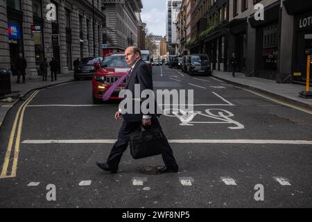 Ein Geschäftsmann spaziert entlang Piccadilly in Mayfair, während der Wind an einem stürmischen Winternachmittag in London, England, Großbritannien, seine violette Anzug-Krawatte weht Stockfoto