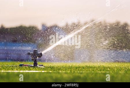 Automatischer Rasenregner, der grünes Gras in einem Stadion bewässert. Bewässerungssystem. Stockfoto