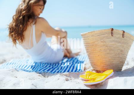 Nahaufnahme einer eleganten Frau am Meer mit Strohbeutel, Flipflops und gestreiftem Handtuch. Stockfoto