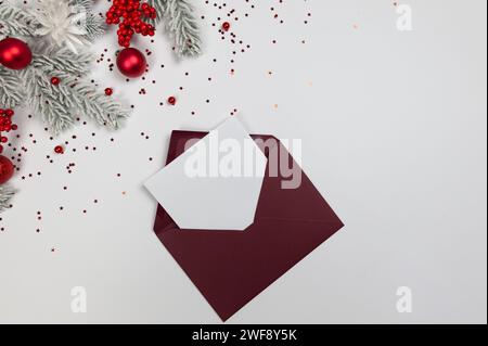 Weihnachtskomposition, roter Umschlag, Tannenzweige, rote Beeren, Kugeln und Sterne Konfetti auf weißem Hintergrund. Stockfoto