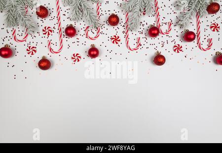 Weihnachtskomposition, Tannenzweige, Bonbons, runde Bonbons, rote Kugeln, Sternenkonfetti auf weißem Hintergrund. Stockfoto