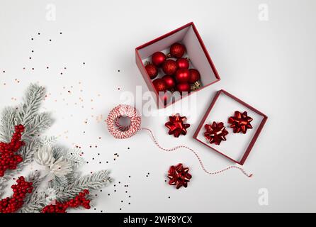 Weihnachtskomposition, Tannenzweige, rote Beeren, Kugeln und Sterne Konfetti auf weißem Hintergrund. Weihnachtsgeschenk-Verpackung, rote Bänder, Geschenkbox. Stockfoto