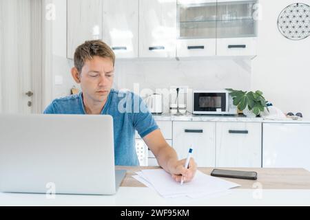 Fernunterricht, Online-Lektion. Zielgerichteter, intelligenter männlicher Student, der aus der Ferne mit einem Laptop studiert und sich während eines Online-Vortrags Notizen macht Stockfoto