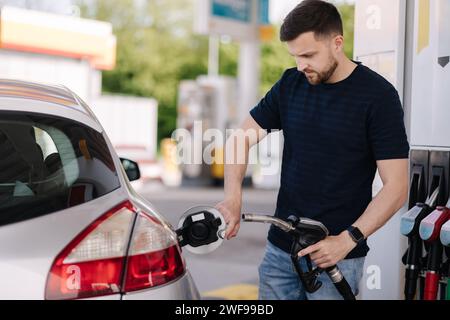 Ein gutaussehender bärtiger Mann betankt das Auto an der Selbstbedienungs-Tankstelle. Benzinkonzept Stockfoto