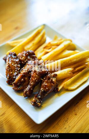 Gebackene Hähnchenflügel und Beine mit Pommes frites auf einem Teller. Stockfoto
