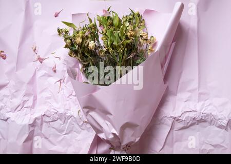 Ein Blumenstrauß mit getrockneten Blumen liegt auf rosafarbenem Geschenkpapier, verwelkte Blumen, alte Blumen Stockfoto