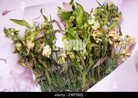 Ein Blumenstrauß mit getrockneten Blumen liegt auf rosafarbenem Geschenkpapier, verwelkte Blumen, alte Blumen Stockfoto