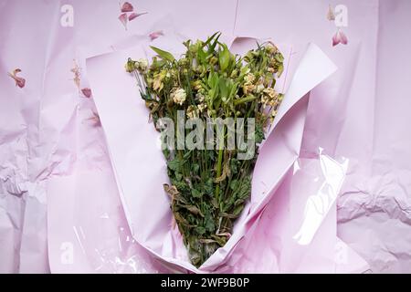 Ein Blumenstrauß mit getrockneten Blumen liegt auf rosafarbenem Geschenkpapier, verwelkte Blumen, alte Blumen Stockfoto