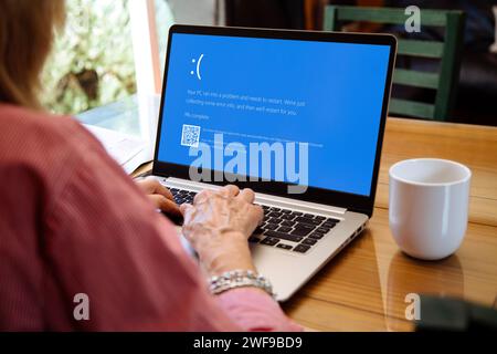 Frau mit Laptop, die auf dem Monitor den blauen Bildschirm des Todes oder BSOD anzeigt. Fehlerhaftes Microsoft-Betriebssystem Windows 10. Stockfoto