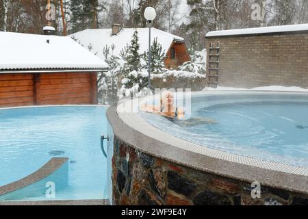 Eine ältere Frau nimmt im Winter Wasserbehandlungen in einem warmen Hydromassagebecken im Freien auf. Glückliche Frau, die sich im Pool erholt. Stockfoto