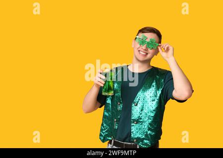 Junger Mann in Brille mit Bier auf gelbem Hintergrund. St. Patrick's Day-Feier Stockfoto