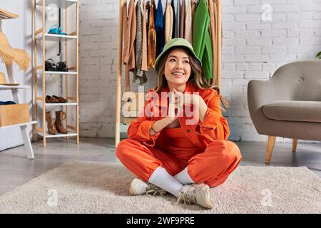 Kreativer asiatischer Designer mit panamahut und oranger Kleidung auf dem Boden in einem privaten Modestudio Stockfoto