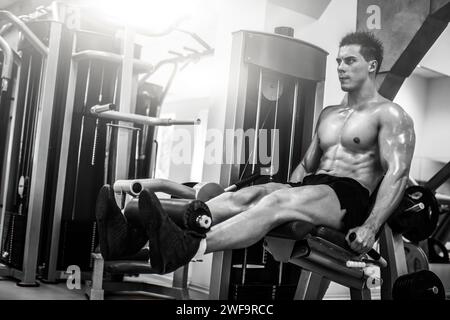 Starker muskulöser Mann, der Beine mit Maschine in einem modernen Fitnessstudio macht Stockfoto