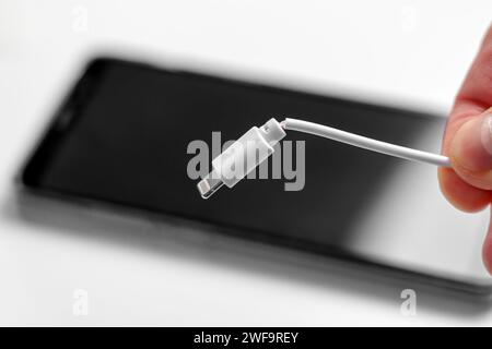 Beschädigtes Ladekabel in der Hand mit Smartphone Nahaufnahme. Fehlerhaftes Elektronikkonzept Stockfoto