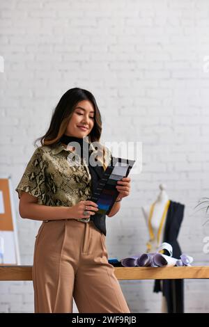 Fröhliche asiatische Kleidung Stylist mit Farbmustern in privatem Modeatelier, Inspiration Stockfoto