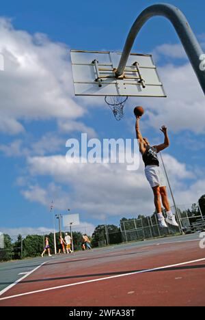 Ein Mann, der Basketballkleidung trägt, springt hoch, während er den Basketball hält, um ihn in den Korb zu tauchen. Stockfoto