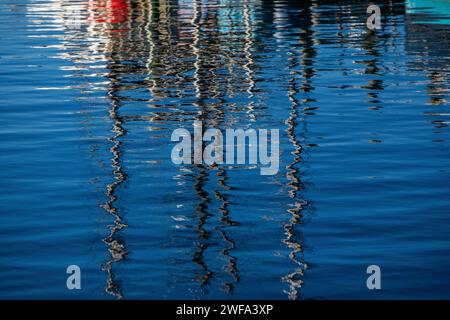 Das ruhige blaue Wasser erzeugt ein faszinierendes abstraktes Muster, das die verzerrte Silhouette und Lichter von Booten in der Abenddämmerung reflektiert. Stockfoto