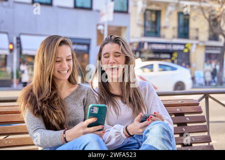 Zwei junge Freunde, die Spaß beim Anschauen des Telefons haben, sehen sich online Videos an und halten das Mobiltelefon in legeren Kleidern. Zwei Freundinnen haben Spaß miteinander Stockfoto