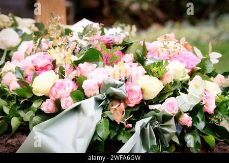 Trauerblumenkranz aus rosa und gelben Rosen und graugrünem Band auf einem Grab nach einer Beerdigung Stockfoto