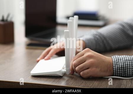 Mann, der Kabel in den WLAN-Router an einem Holztisch drinnen steckt, Nahaufnahme Stockfoto