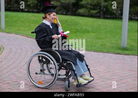 Eine weiße Frau im Rollstuhl hält ihr Diplom und weint vor Freude draußen. Stockfoto