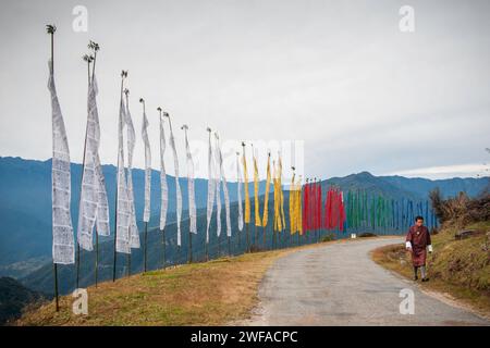 Bhutanese spazieren an hohen Gebetsfahnen auf Pfählen entlang einer Landstraße im Bumthang Valley, Bhutan, Asien Stockfoto