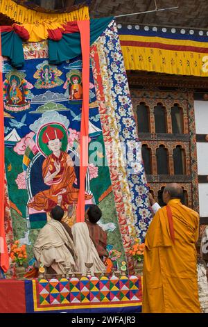 Lama beaufsichtigt zwei Mönche in traditioneller Kleidung, die zu Beginn des jährlichen religiösen tsechu-Festivals eine gestickte Platte aufbringen. Stockfoto